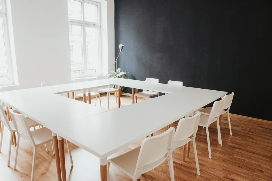 Große weiße Tafel mit Stühlen vor einer dunklen Wand